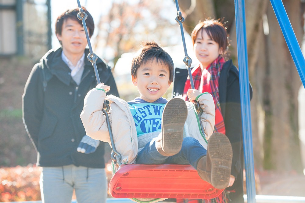  - ブランコで楽しく遊ぶ男の子を&nbsp;優しく見守る お父さんとお母さん